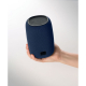 Haut-parleur bleu tenu dans une main, montrant son format compact, son revêtement en tissu, les commandes sur le dessus et la pe Haut-parleur bleu tenu dans une main, montrant son format compact, son revêtement en tissu, les commandes sur le dessus et la pe