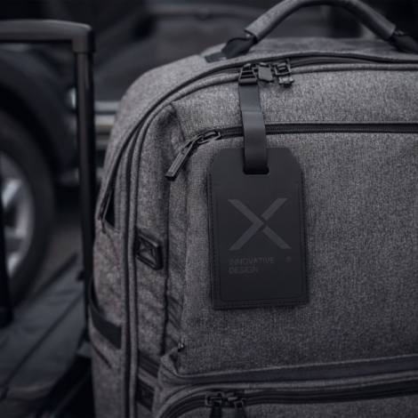 Étiquette de bagage noire personnalisée fixée à un sac de voyage gris.