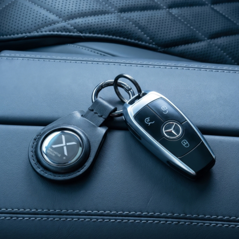 Porte-clés connecté noir personnalisé accroché à une clé de voiture sur un siège en cuir.