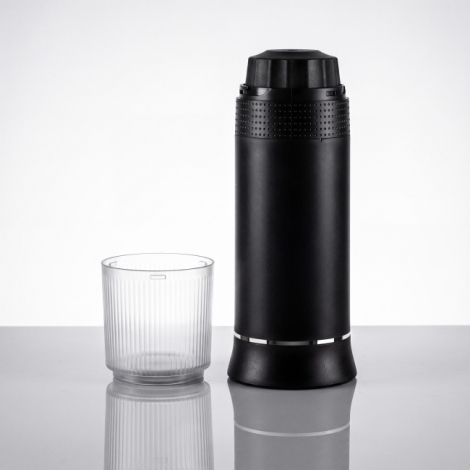 Machine à expresso portable noire retournée avec gobelet transparent amovible posé à côté.