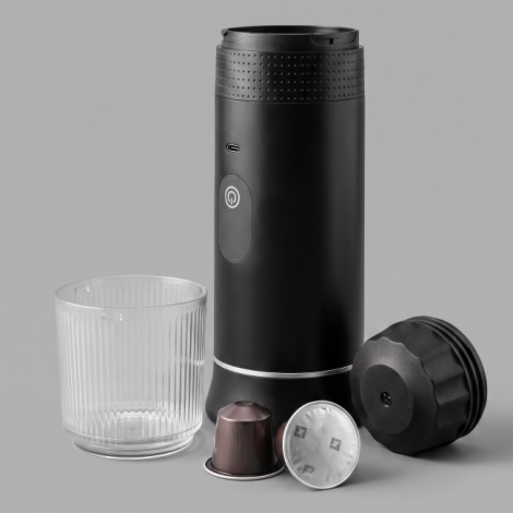 Machine à expresso portable noire accompagnée de son gobelet transparent, de deux capsules de café et d'un porte-capsule.