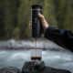 Machine à expresso portable électrique noire utilisée en extérieur pour verser du café dans un gobelet transparent au bord d'une Machine à expresso portable électrique noire utilisée en extérieur pour verser du café dans un gobelet transparent au bord d'une