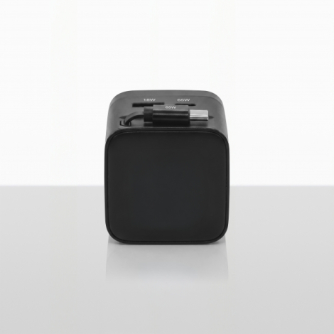 Vue de face d'un adaptateur de voyage universel noir, de forme cubique aux angles arrondis, avec câble USB-C intégré rangé sur l