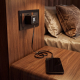 Adaptateur de voyage noir branché sur une prise murale dans une chambre, avec marquage lumineux blanc sur la face avant et câble