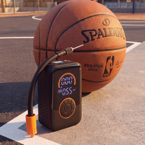 Mini-compresseur électrique noir posé sur un terrain de basketball à côté d'un ballon orange, avec flexible de gonflage et aigui
