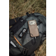 Un chauffe-main noir relié par un câble à un smartphone marron est posé sur un sac à dos gris et noir, dans l'herbe.