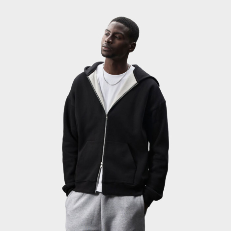 Mannequin homme portant un sweat zippé noir à capuche, ouvert sur un t-shirt blanc. La doublure claire de la capuche, la fermetu