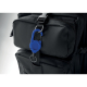 Un porte-badge rétractable bleu est accroché à une sangle d’un sac à dos noir, avec son boîtier circulaire et son anneau métalli