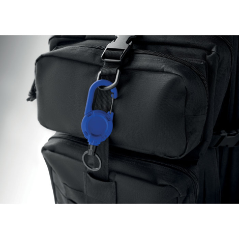 Un porte-badge rétractable bleu est accroché à une sangle d’un sac à dos noir, avec son boîtier circulaire et son anneau métalli