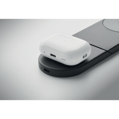 Gros plan sur un boîtier d'écouteurs sans fil blanc posé sur la base de recharge noire, avec un port USB-C visible sur le bord d