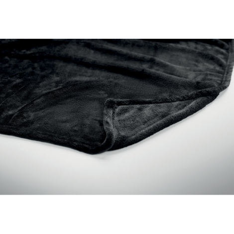 Gros plan sur un coin replié de la couverture noire, montrant sa texture polaire douce, ses bordures cousues et son épaisseur.