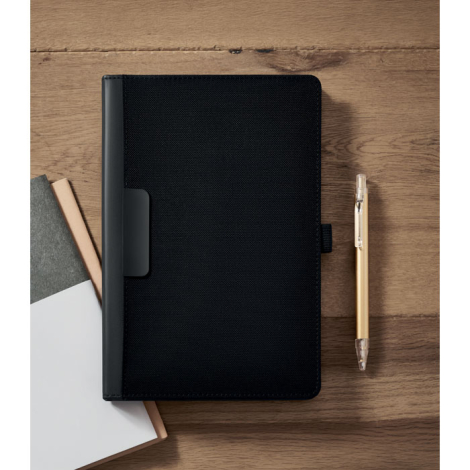Conférencier A5 noir fermé, posé sur une table en bois à côté d'un stylo beige et de plusieurs carnets partiellement visibles.