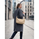 Une femme portant un manteau gris marche dans une rue urbaine avec un sac beige souple porté à l'épaule, muni d'une large bandou Une femme portant un manteau gris marche dans une rue urbaine avec un sac beige souple porté à l'épaule, muni d'une large bandou