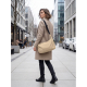 Une femme en manteau beige porte un sac urbain beige en bandoulière sur le côté, dans une rue bordée d'immeubles, avec la sangle Une femme en manteau beige porte un sac urbain beige en bandoulière sur le côté, dans une rue bordée d'immeubles, avec la sangle