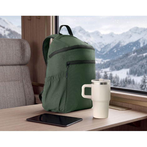 Sac à dos vert posé sur une table en bois près d'une fenêtre donnant sur un paysage de montagnes enneigées, accompagné d'un gobe