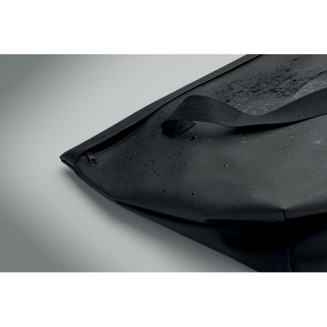 Vue rapprochée du tissu noir du sac recouvert de gouttelettes d'eau, avec une anse en sangle et une partie de la fermeture zippé