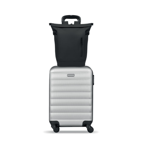 Sac à dos noir posé sur une valise rigide argentée à roulettes, avec la poignée télescopique de la valise visible derrière le sa