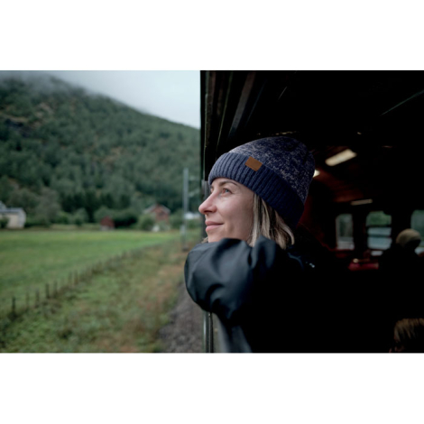 Une femme portant un bonnet bleu à revers avec un petit patch marron regarde le paysage depuis la fenêtre d'un train.