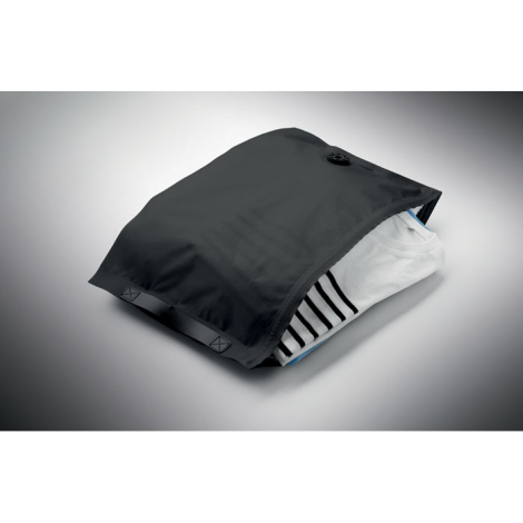 Sac de compression noir entrouvert, contenant plusieurs vêtements pliés, dont un vêtement blanc et un tissu à rayures noires et 
