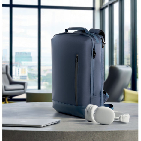 Sac à dos bleu marine posé sur une table, à côté d'un ordinateur portable argenté et d'un casque audio blanc, dans un espace vit