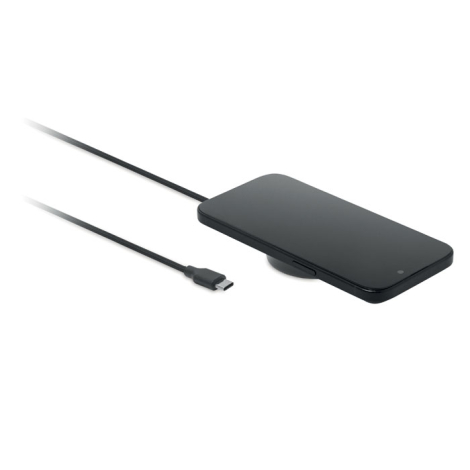 Smartphone noir posé à plat, écran vers le haut, sur un chargeur magnétique rond partiellement visible sous l'appareil. Le câble