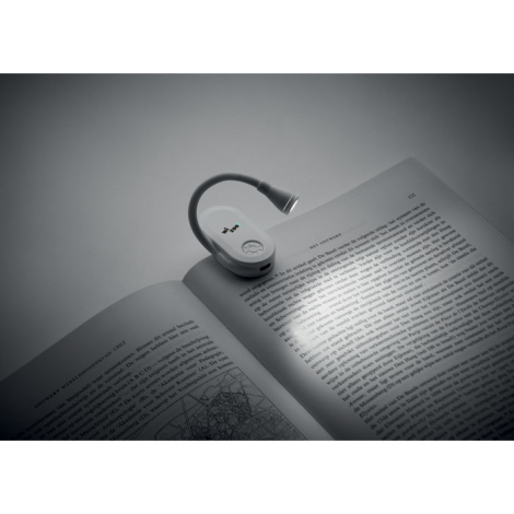 Lampe de lecture grise fixée sur les pages d'un livre ouvert, avec bras flexible courbé et tête lumineuse orientée vers le texte