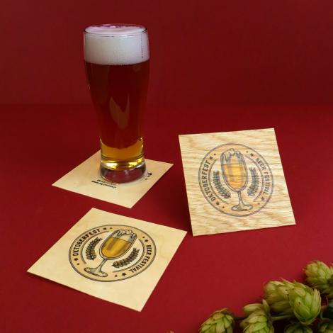 Trois sous-verres carrés en bois clair personnalisés, disposés sur fond rouge. Deux sont posés à plat, le troisième légèrement i