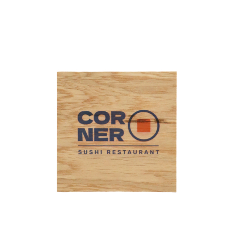 Sous-verre carré en bois brun clair, posé à plat sur fond blanc, avec veinage horizontal marqué et personnalisation centrale com