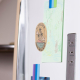 Élément ovale en bois clair fixé sur la porte blanche d'un réfrigérateur, avec textes noirs et colorés et illustration. Vue de t