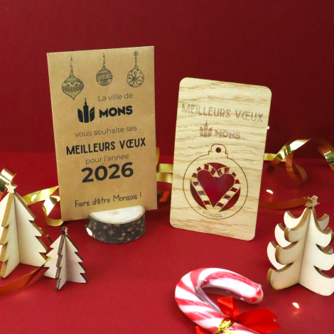 Carte de vœux en bois clair avec boule de Noël détachable, flocon ajouré et logo personnalisé. Présentée sur fond blanc près d'u