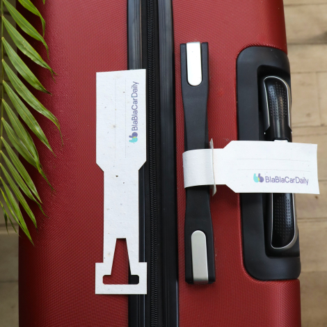 Deux étiquettes de bagage blanches en papier moucheté avec logo BlaBlaCar Daily, sur une valise rouge. L'une est fixée à la poig