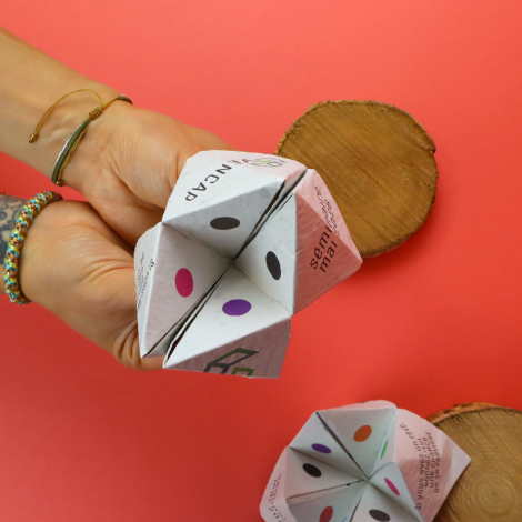 Cocotte en papier personnalisée tenue ouverte dans les mains, avec pastilles colorées et textes sur les rabats. Fond rouge et se