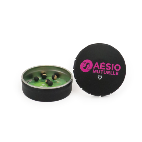Boîte clic-clac ronde noire personnalisée AESIO Mutuelle, ouverte avec des graines de pois de cœur et son couvercle marqué en ro