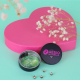 Boîte ronde noire personnalisée AESIO Mutuelle, ouverte avec des graines de pois de cœur, devant une grande boîte rose en forme Boîte ronde noire personnalisée AESIO Mutuelle, ouverte avec des graines de pois de cœur, devant une grande boîte rose en forme