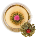 Vue de dessus d'une fleur de thé épanouie au cœur rose dans une tasse en verre remplie d'infusion dorée, avec une seconde fleur 