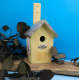 Nichoir à oiseaux en bois naturel personnalisé avec logo ER gravé sur la façade, toit métallique gris et trou d'envol rond. Prés