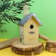 Nichoir à oiseaux en bois naturel avec toit métallique, ouverture circulaire et support de fixation arrière. Présenté sur rondin