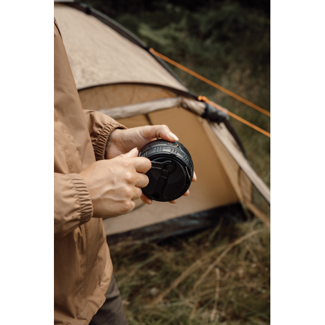 Une personne manipule la manivelle de la lanterne noire devant une tente de camping installée en pleine nature.
