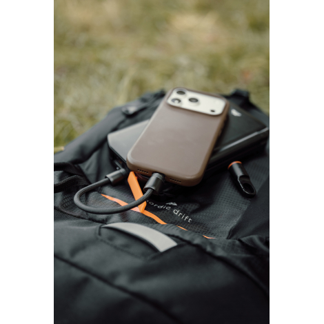 Smartphone posé sur un chargeur noir pliable, avec câble de charge tressé connecté au téléphone et mousqueton détaché placé à cô