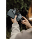 Une femme en veste claire tient un smartphone contre un chargeur noir pliable et approche le connecteur du câble de charge tress Une femme en veste claire tient un smartphone contre un chargeur noir pliable et approche le connecteur du câble de charge tress