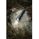 Lampe torche noire allumée, posée sur un rocher couvert de mousse en pleine nature, projetant un faisceau lumineux blanc sur la 