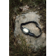 Lampe frontale noire allumée, posée sur un rocher entouré d'herbes et de mousse. Son bandeau élastique est disposé en boucle, av Lampe frontale noire allumée, posée sur un rocher entouré d'herbes et de mousse. Son bandeau élastique est disposé en boucle, av