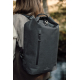 Femme photographiée de dos en extérieur, portant un sac à dos noir à fermeture enroulable, avec poche zippée verticale et bretel Femme photographiée de dos en extérieur, portant un sac à dos noir à fermeture enroulable, avec poche zippée verticale et bretel