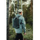 Homme photographié de dos dans une forêt, portant un sac à dos noir à fermeture enroulable, avec bretelles noires et petit motif Homme photographié de dos dans une forêt, portant un sac à dos noir à fermeture enroulable, avec bretelles noires et petit motif