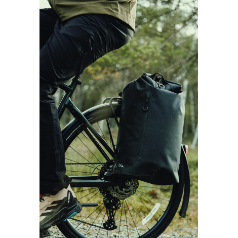 Vue rapprochée d’un sac noir fixé sur le côté d’un vélo, à hauteur de la roue arrière, avec fermeture enroulable et poche zippée