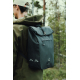 Homme photographié de profil et de dos en forêt, portant un sac à dos noir à rabat, avec deux motifs géométriques clairs sur le Homme photographié de profil et de dos en forêt, portant un sac à dos noir à rabat, avec deux motifs géométriques clairs sur le