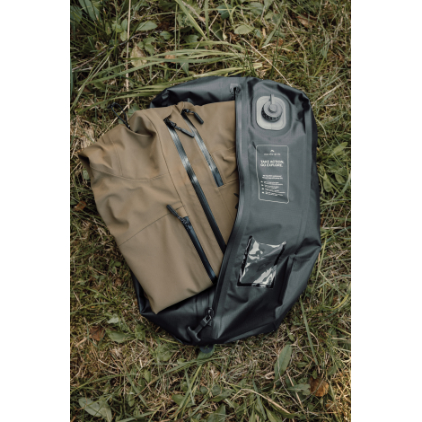 Sac de compression noir ouvert et posé dans l'herbe, contenant un sac beige à plusieurs fermetures zippées. La valve ronde, les 
