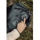 Gros plan sur la valve ronde ouverte du sac de compression noir posé dans l'herbe, avec une main appuyant sur son mécanisme et u