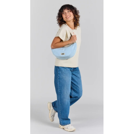 Femme portant à l'épaule le sac demi-lune Inès bleu azur, avec bandoulière écrue réglable et étiquette personnalisée avec logo s