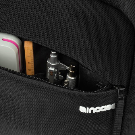 Gros plan sur une poche zippée du sac à dos noir, ouverte pour révéler plusieurs petits rangements contenant notamment une règle